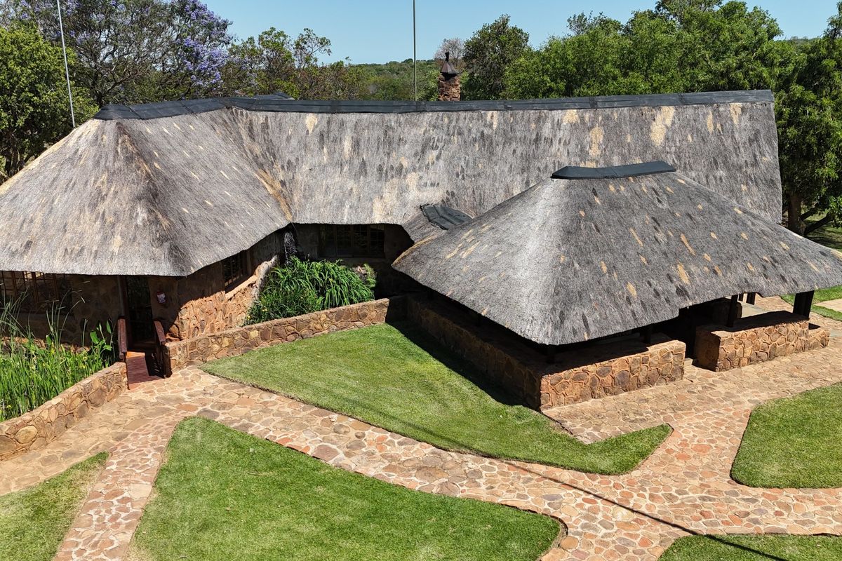 Aerial view of a farm-style residence featuring traditional thatched roofing, stone-clad exterior walls, and well-maintained stone pathways leading through the garden.