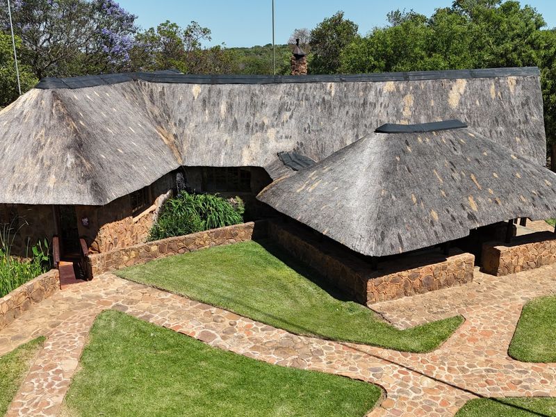 Aerial view of a farm-style residence featuring traditional thatched roofing, stone-clad exterior walls, and well-maintained stone pathways leading through the garden.