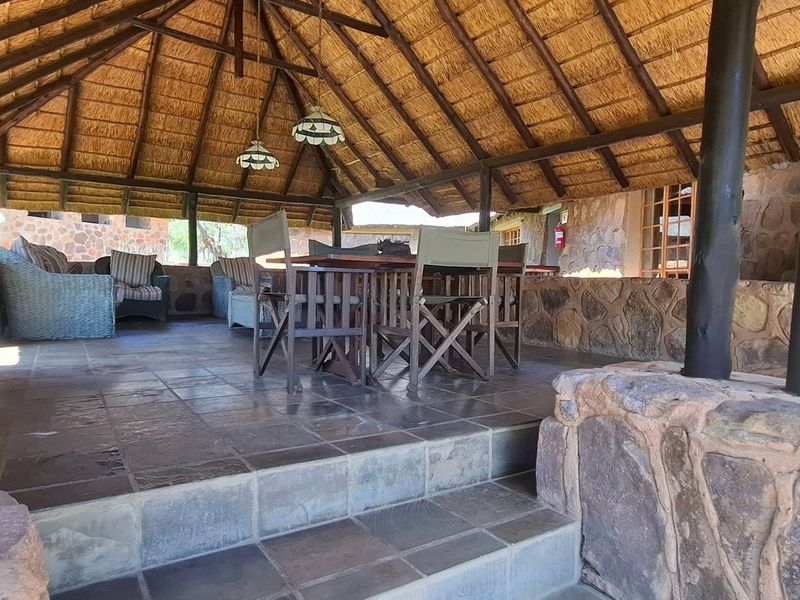 A spacious covered patio featuring a traditional thatched roof, rustic stone walls, and durable tiled flooring, ideal for outdoor relaxation and entertainment.