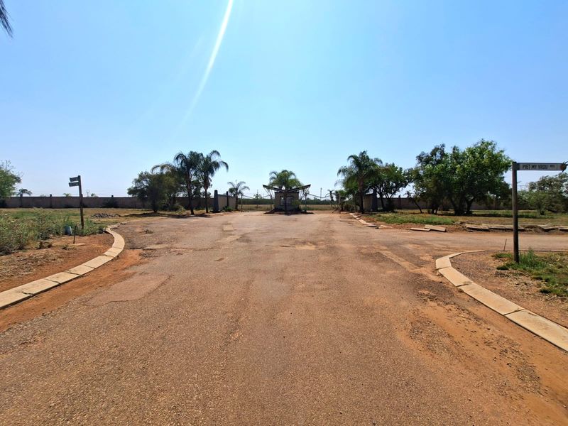 View of the entrance to the residential property featuring an asphalt driveway, security gate, and perimeter wall.