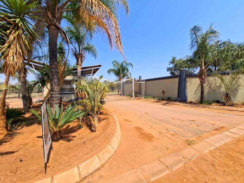 Front entrance view of the residential property featuring a secure gated access point, perimeter walling, and established garden landscaping.