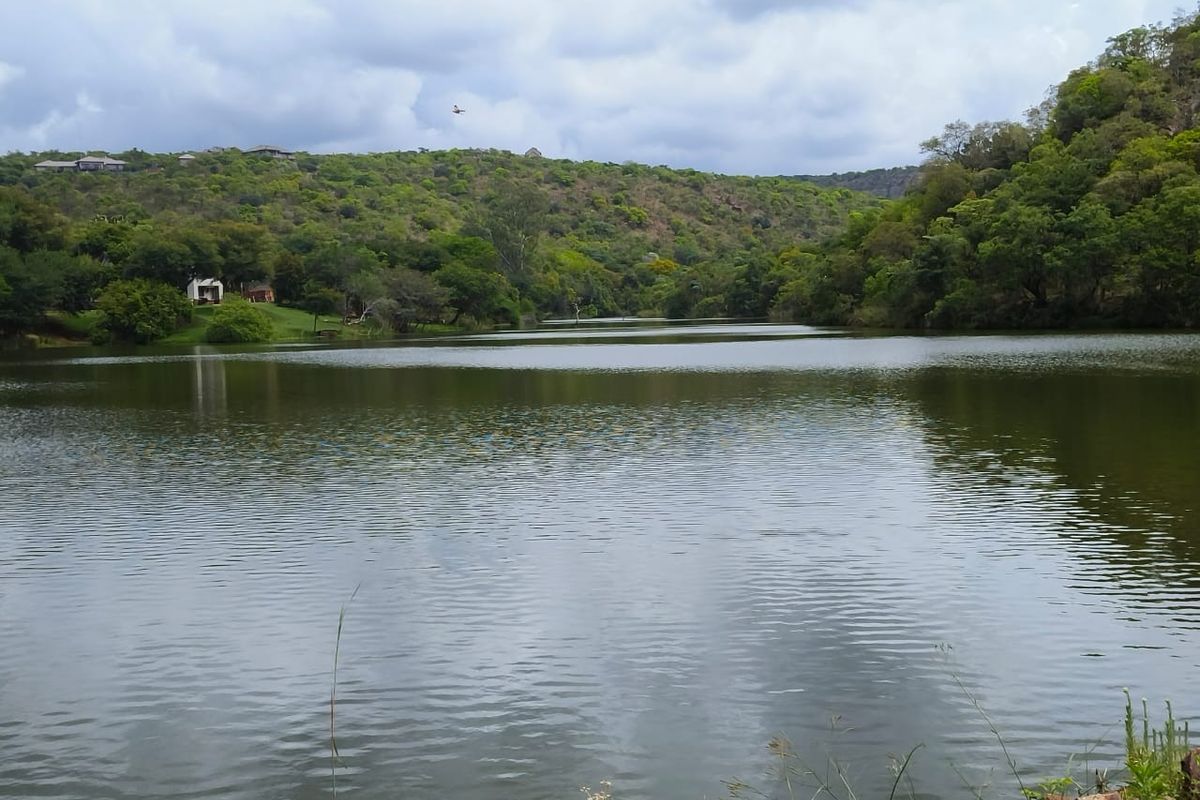 A scenic view of a tranquil lake surrounded by lush green hills and natural vegetation, offering a peaceful landscape setting.