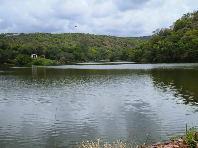 A scenic view of a tranquil lake surrounded by lush green hills and natural vegetation, offering a peaceful landscape setting.