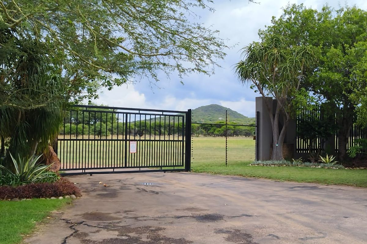 A secure gated entrance to a residential property featuring a paved driveway, perimeter fencing, and established trees with scenic mountain views.