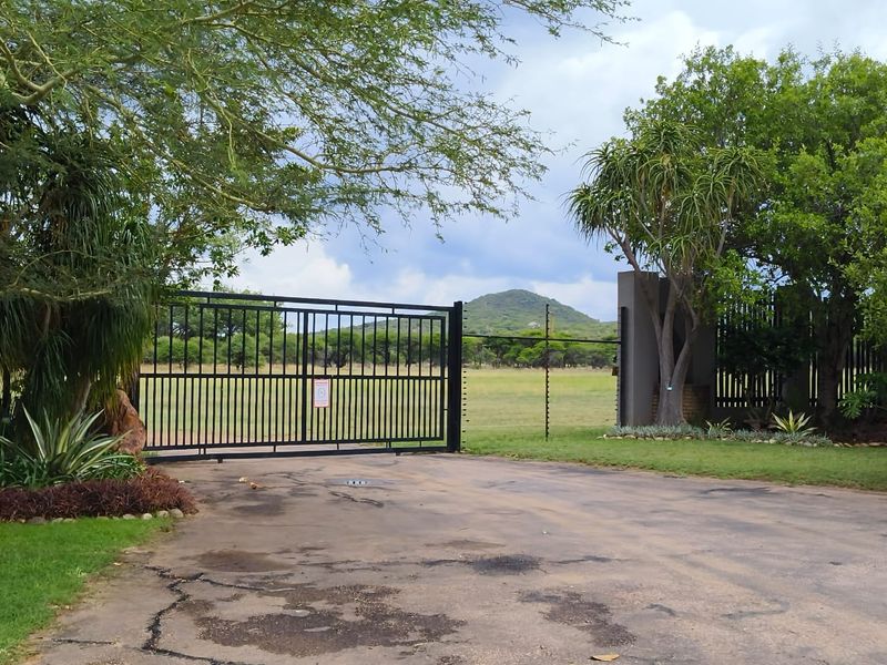 A secure gated entrance to a residential property featuring a paved driveway, perimeter fencing, and established trees with scenic mountain views.