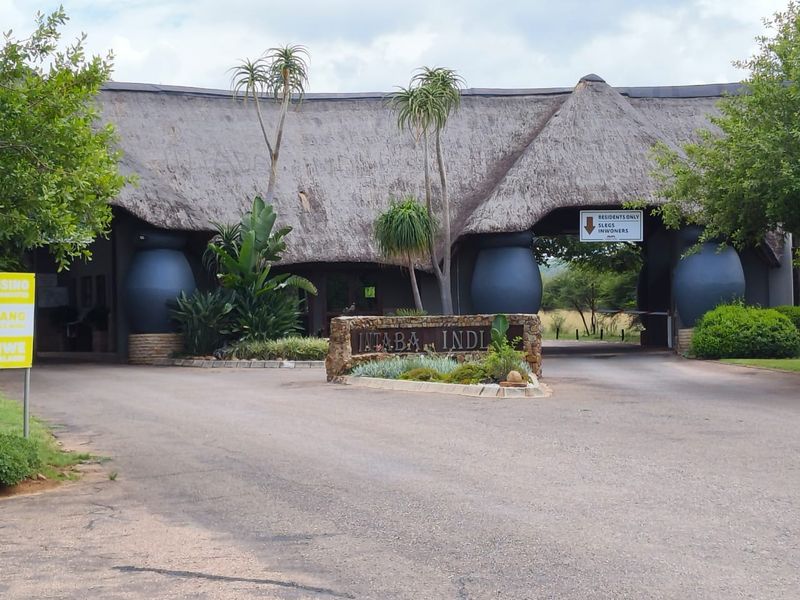 The entrance to Intaba Indlu estate featuring a distinctive thatched roof gatehouse, stone signage, and a paved driveway.