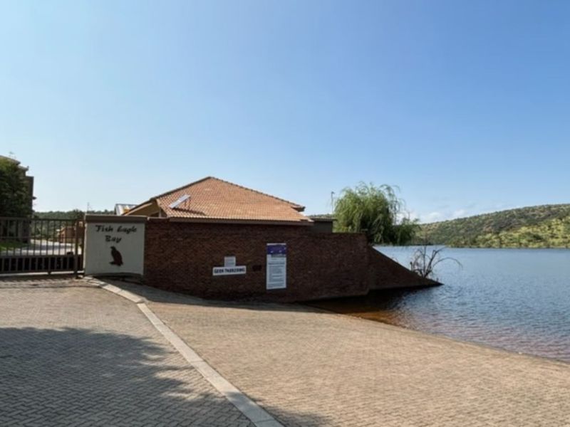 Entrance view of the property featuring a paved driveway, security gate, and direct access to the waterfront.
