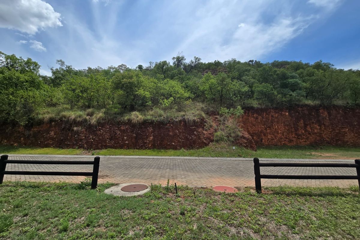 A view of the paved street frontage and adjacent embankment, featuring established timber fencing and utility access points on a vacant residential plot.