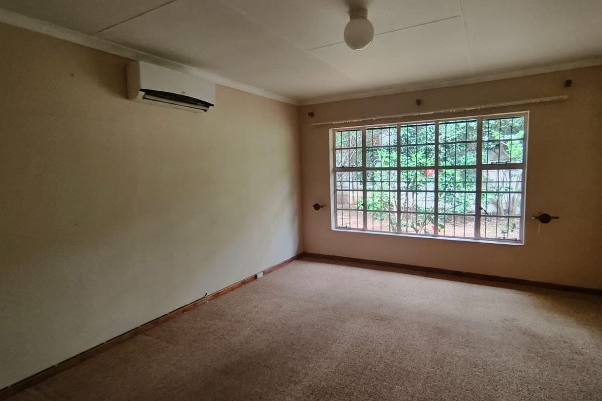 An empty bedroom featuring carpet flooring, a wall-mounted air conditioning unit, and a large window with security bars.