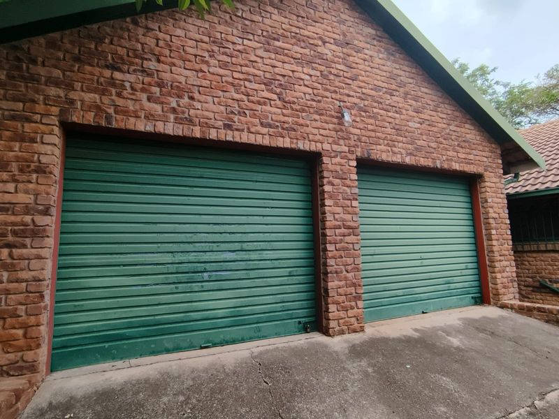 A double garage featuring face brick exterior walls and green roller doors, with a concrete driveway showing minor surface cracking.