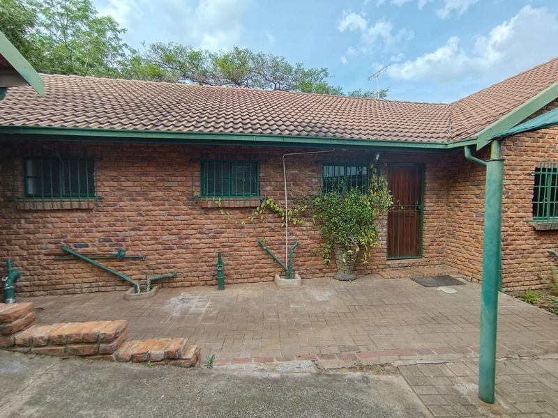 Rear exterior view of a brick house featuring a paved patio area, tiled roof, and security-fitted windows and doors.