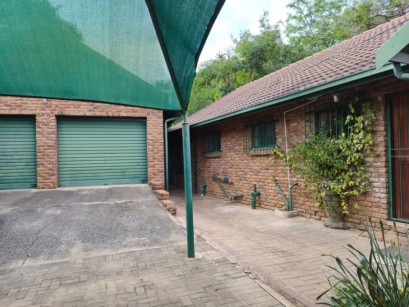 Exterior view of a brick-faced house featuring a double garage, paved driveway, and a shade sail structure over the parking area.