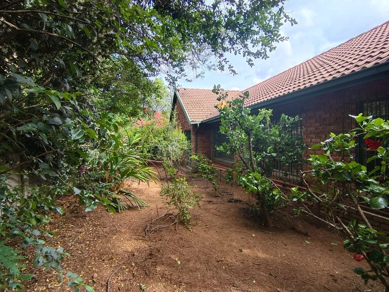 A view of the rear exterior of the house featuring a brick facade, tiled roof, and a garden area with mature trees and shrubs.