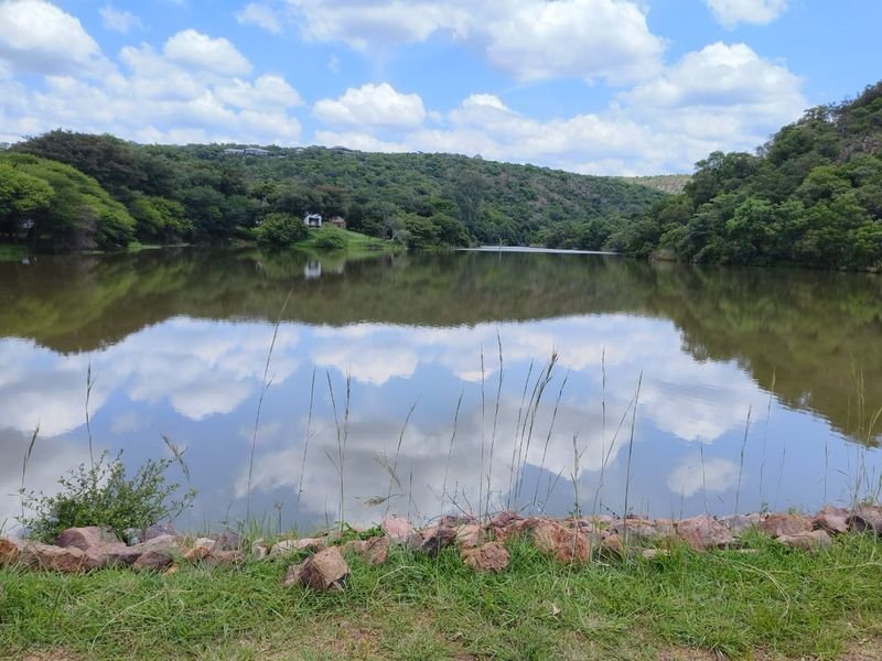 A scenic view of a tranquil lake surrounded by lush green hills and natural vegetation, offering a peaceful landscape setting.