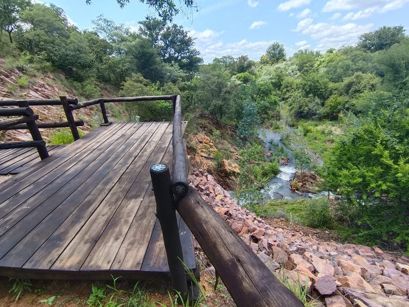 A scenic timber viewing deck overlooking a natural stream and lush, wooded landscape.