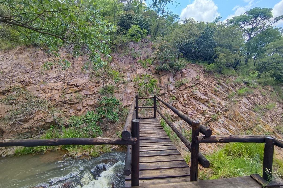 A scenic view of a natural stream and rock formation, featuring a rustic wooden footbridge crossing the water.