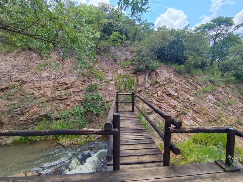 A scenic view of a natural stream and rock formation, featuring a rustic wooden footbridge crossing the water.