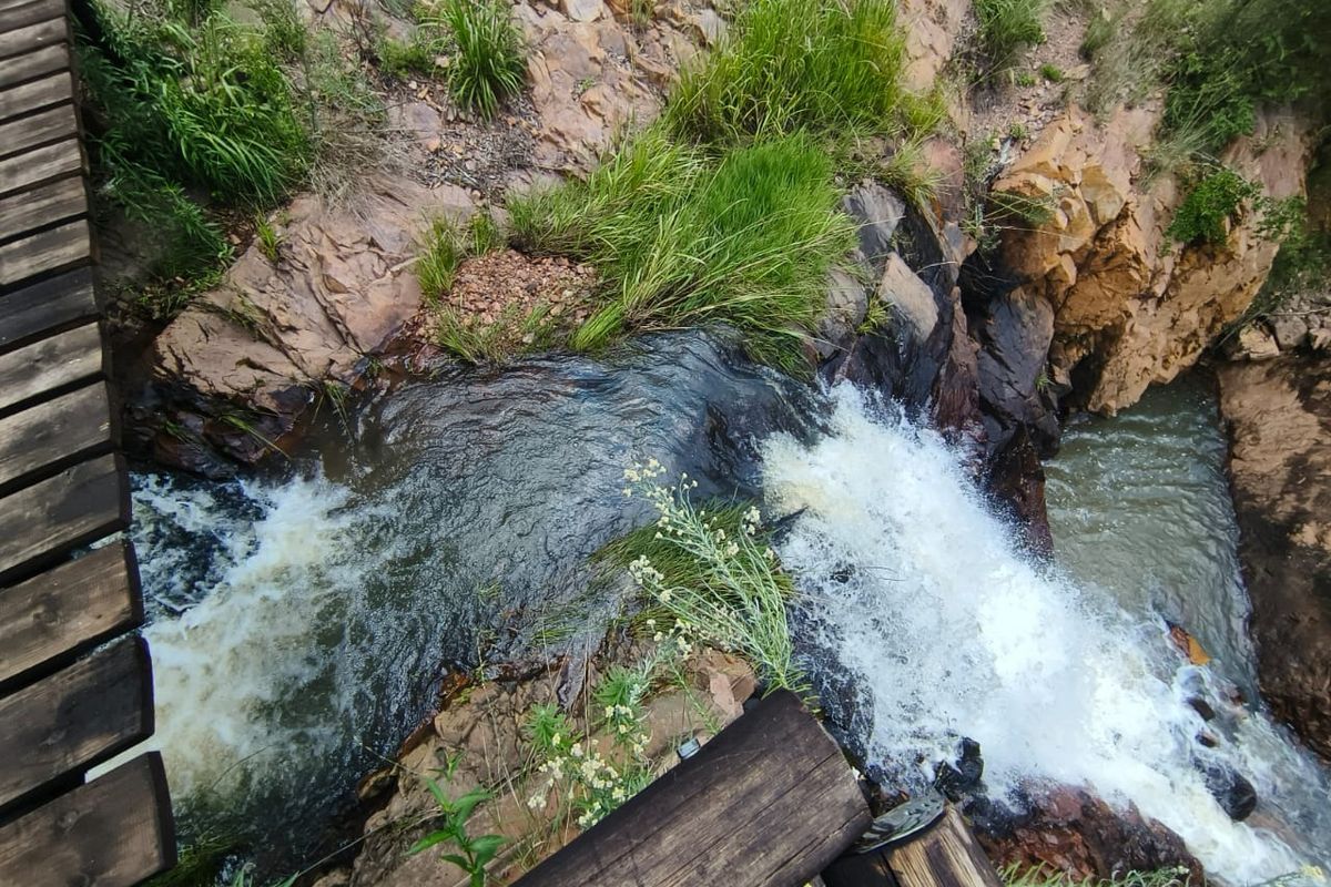 A scenic view of a natural waterfall cascading over rocky terrain, viewed from an adjacent wooden footbridge.