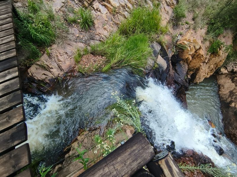 A scenic view of a natural waterfall cascading over rocky terrain, viewed from an adjacent wooden footbridge.