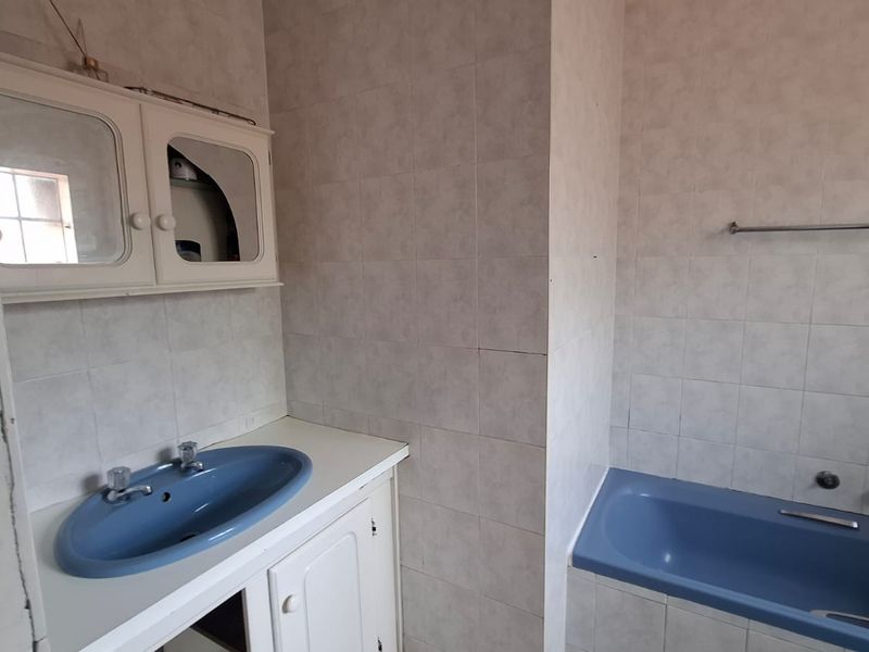 A dated bathroom featuring a blue built-in bathtub and matching vanity basin, with tiled walls and a wall-mounted medicine cabinet.