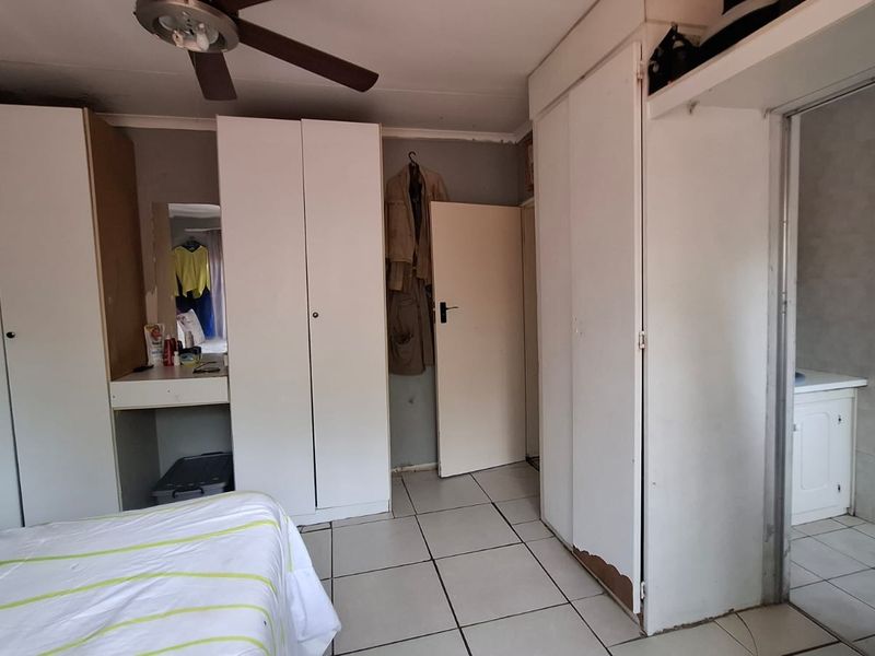 Bedroom featuring built-in cupboards, tiled flooring, and an en-suite bathroom. The space requires cosmetic updates to improve its overall condition.