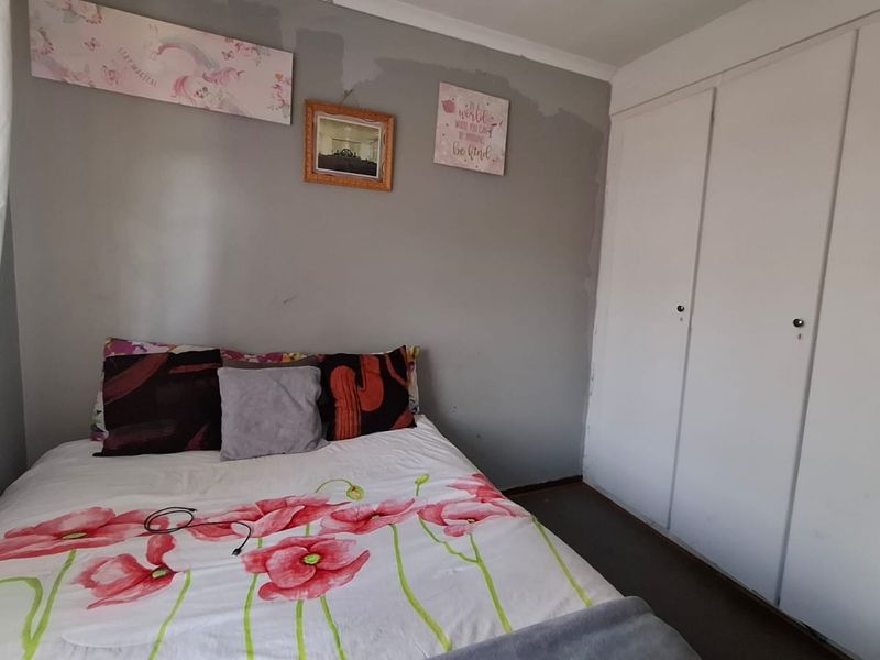 A bedroom featuring built-in cupboards and coving, currently showing signs of wear on the wall surfaces.