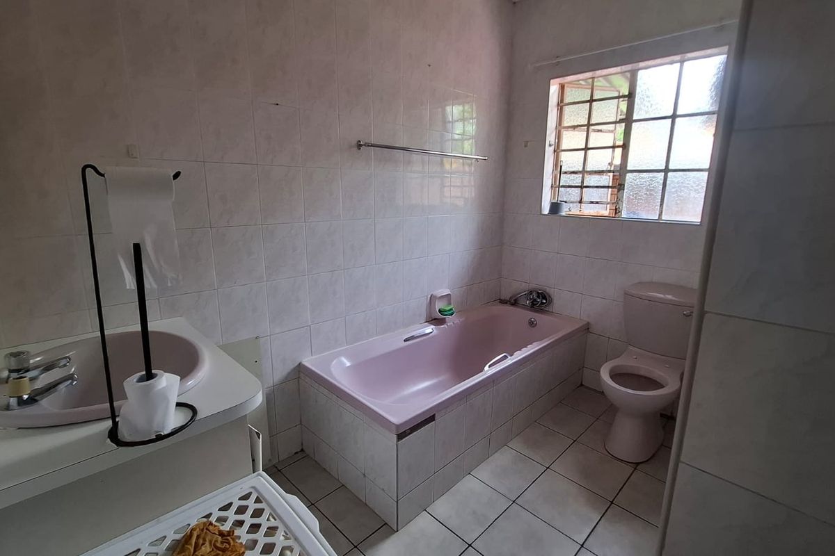 A functional bathroom featuring a built-in bathtub, toilet, and vanity basin with tiled finishes throughout.