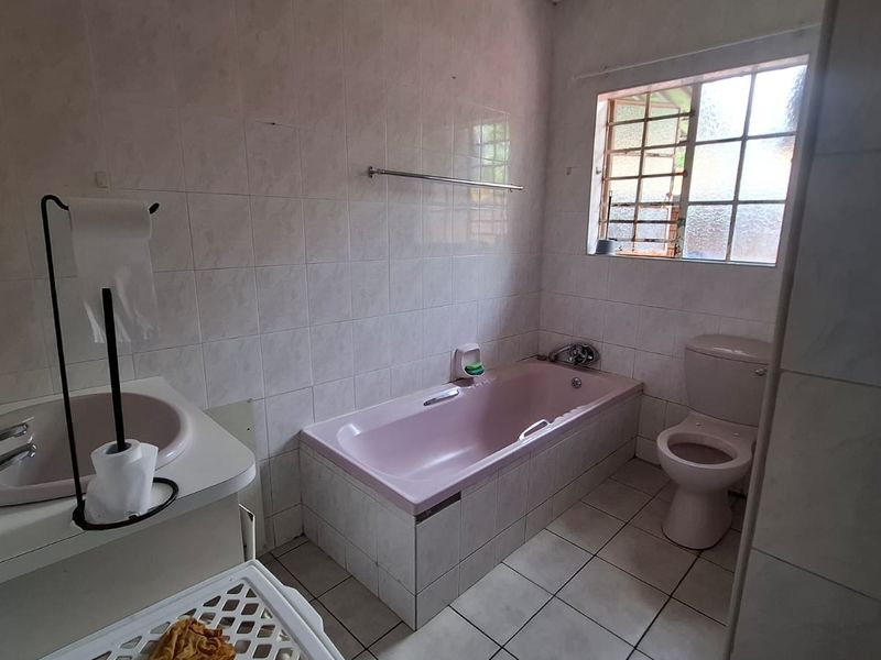 A functional bathroom featuring a built-in bathtub, toilet, and vanity basin with tiled finishes throughout.