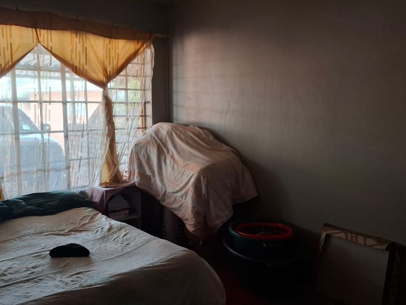 A bedroom featuring a window with security bars, currently used for storage with limited natural light.