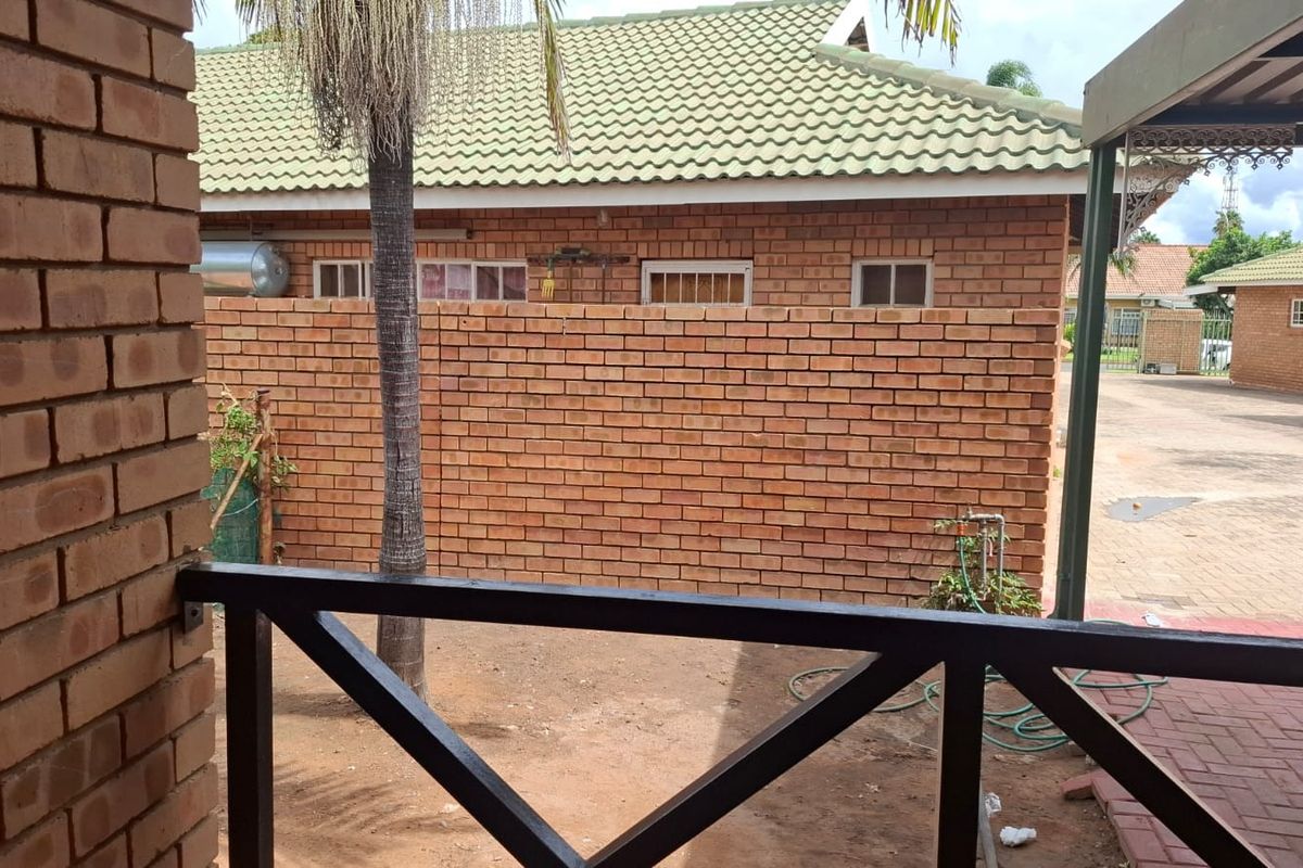 A view of the rear exterior area featuring face brick walls, a tiled roof, and a paved driveway section.