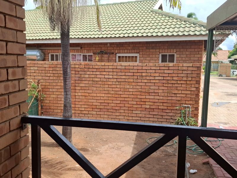 A view of the rear exterior area featuring face brick walls, a tiled roof, and a paved driveway section.