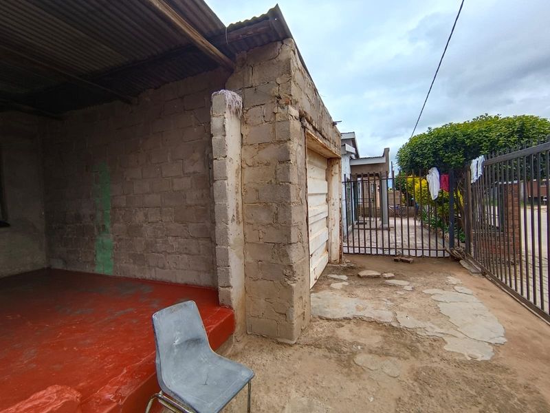 Front exterior view showing a basic structure with concrete block walls, corrugated metal roofing, and a metal security gate entrance.