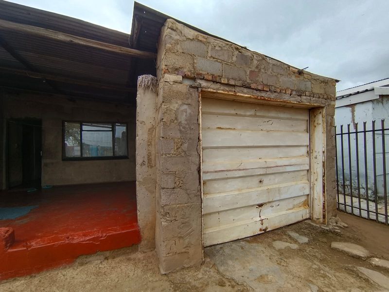 Front exterior view of a property featuring a garage with a metal door and an adjacent covered entrance area with painted concrete flooring.