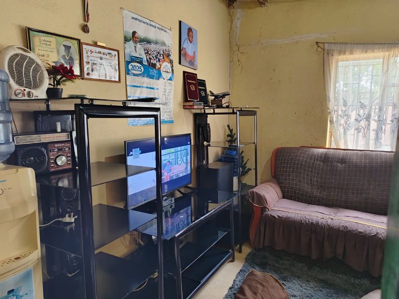 A living room area featuring a window with security bars and visible wall surface deterioration requiring maintenance and cosmetic repair.