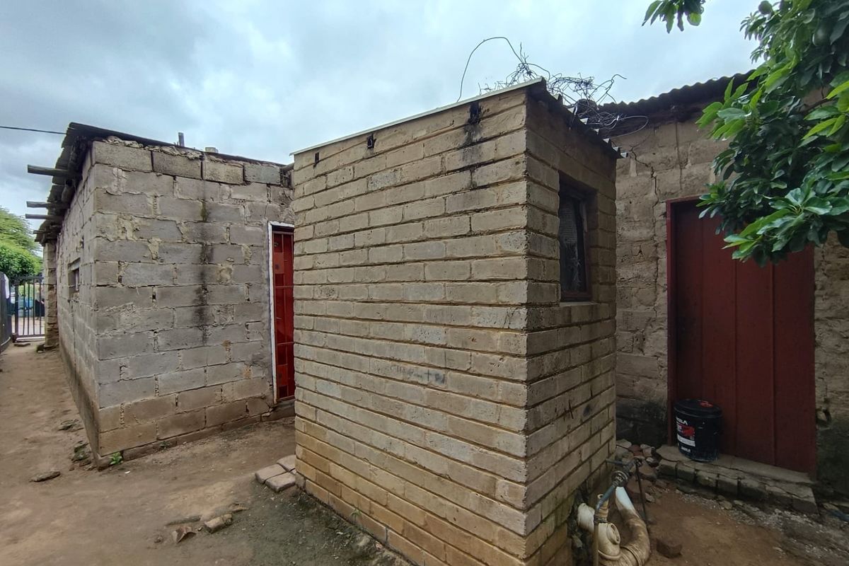 Exterior view of a basic concrete block structure with exposed plumbing and unfinished masonry walls in a rear yard setting.