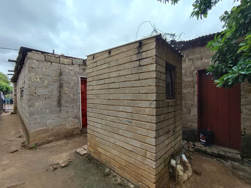 Exterior view of a basic concrete block structure with exposed plumbing and unfinished masonry walls in a rear yard setting.