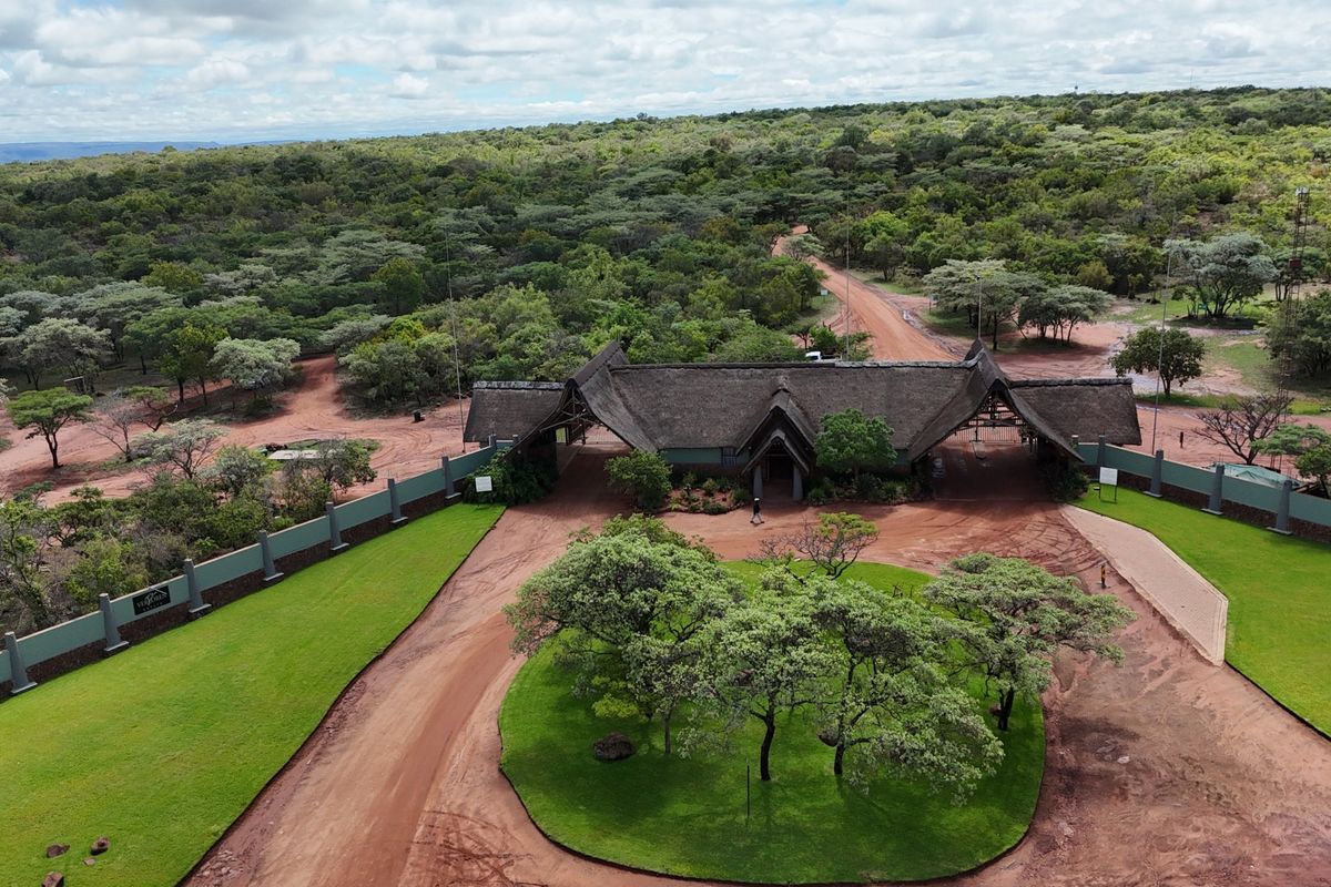 Aerial view of a gated residential estate entrance featuring a thatched roof structure, perimeter walling, and manicured lawns set within a natural bushveld landscape.