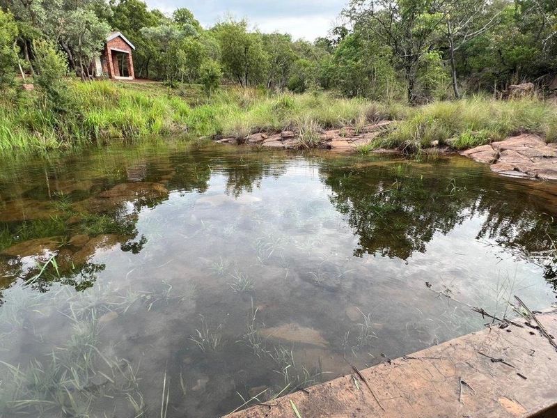 A scenic view of a natural rock pool surrounded by native trees and rocky landscape on the residential property.