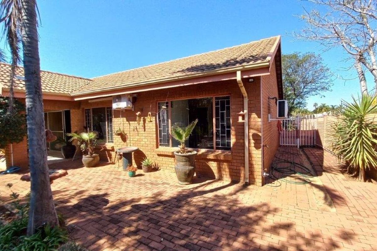 Rear view of the townhouse featuring a brick facade, tiled roof, and a spacious paved patio area.