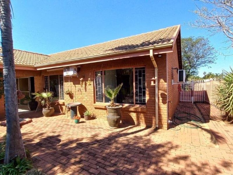 Rear view of the townhouse featuring a brick facade, tiled roof, and a spacious paved patio area.