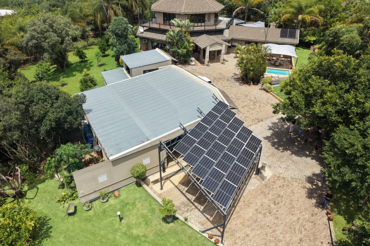 Aerial view of a farm property featuring a main residence, swimming pool, extensive landscaped gardens, and a large ground-mounted solar panel array.
