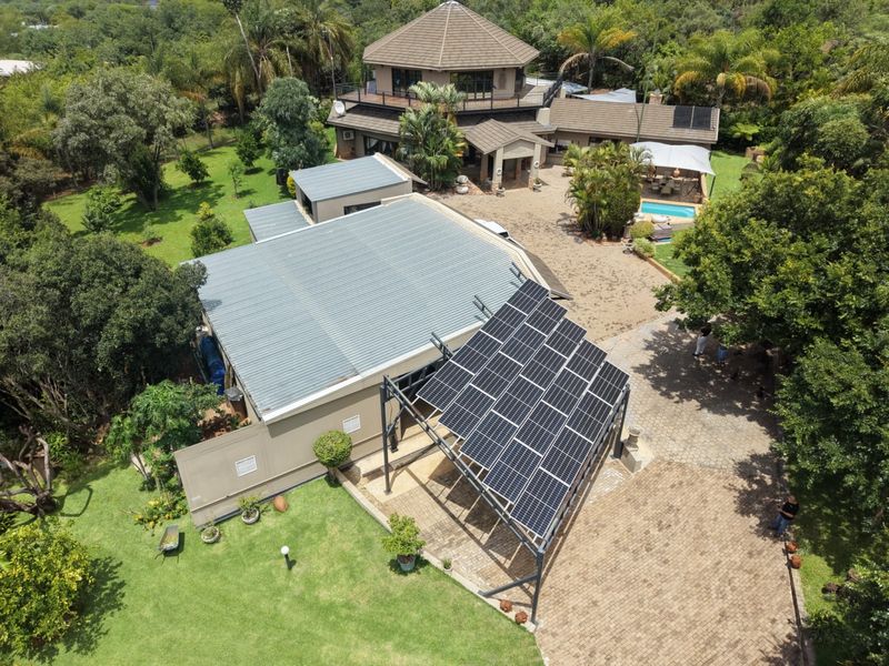 Aerial view of a farm property featuring a main residence, swimming pool, extensive landscaped gardens, and a large ground-mounted solar panel array.