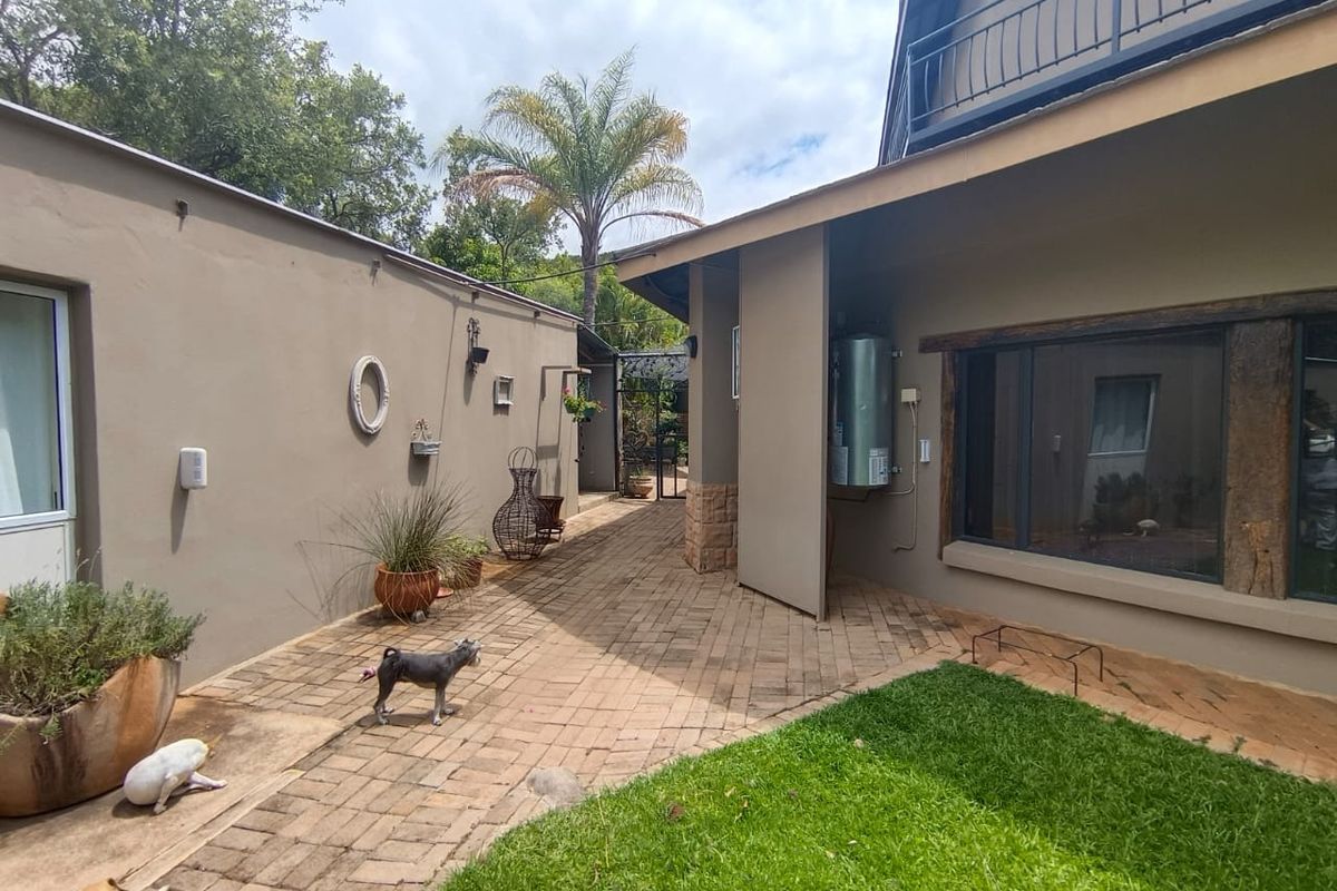 A paved rear courtyard area featuring a mounted electric geyser, stone accents, and access to a balcony above.