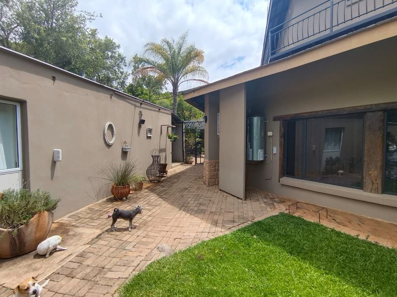 A paved rear courtyard area featuring a mounted electric geyser, stone accents, and access to a balcony above.