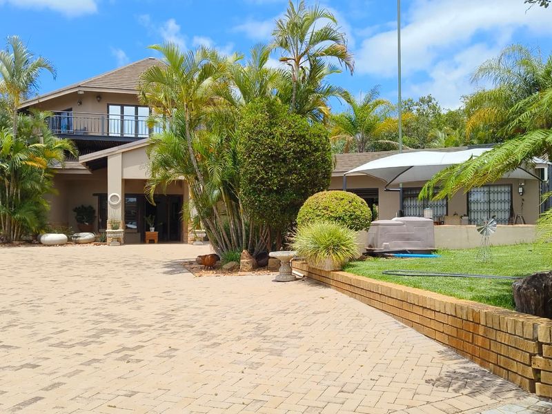 A well-maintained farm property featuring a paved driveway, brick retaining walls, and a multi-level residence with a balcony and established garden.