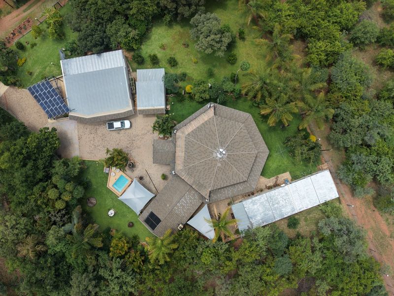 Aerial view of a farm property featuring a main residence with a unique roof design, outbuildings, solar panels, a swimming pool, and landscaped grounds.