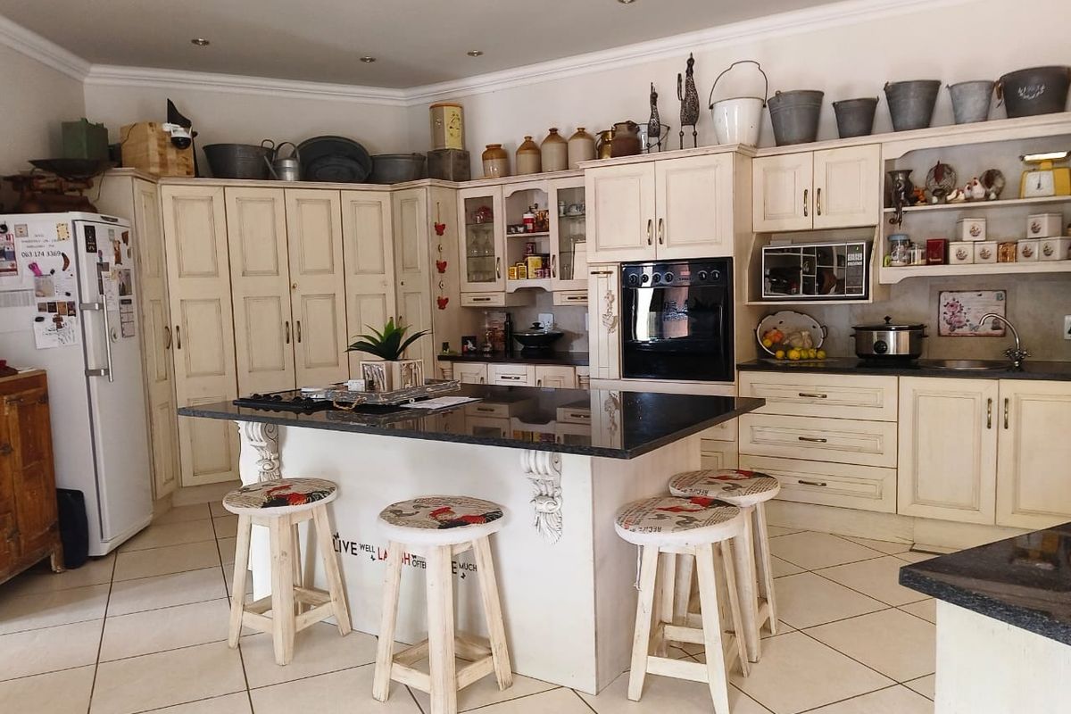 A spacious farmhouse-style kitchen featuring cream cabinetry, a central island with granite countertops, built-in oven, and tiled flooring.