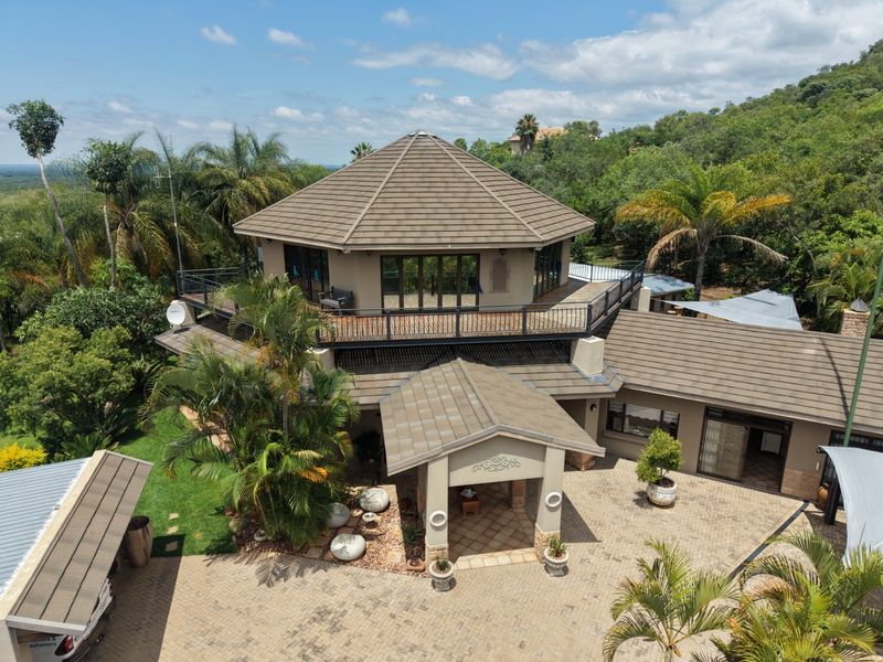 Aerial view of a multi-level farm property featuring a distinctive hexagonal roof design, paved courtyard, and expansive wrap-around balcony with scenic landscape views.