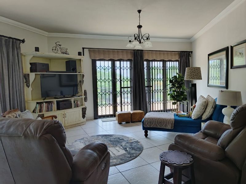 A comfortable living room featuring tiled floors, decorative cornicing, and large sliding glass doors with security gates leading to the exterior.