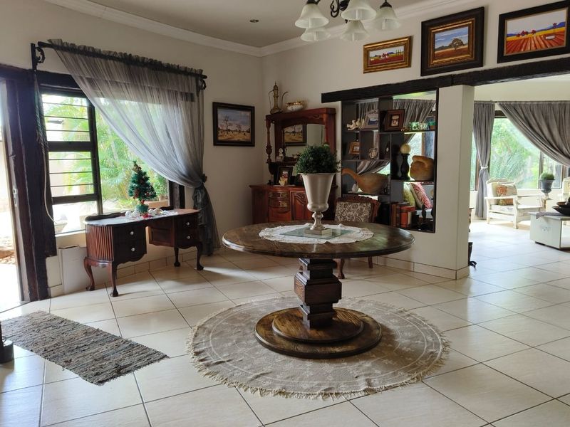 A spacious living area featuring tiled flooring, recessed lighting, and a built-in shelving unit, with an open-plan layout connecting to adjacent living spaces.